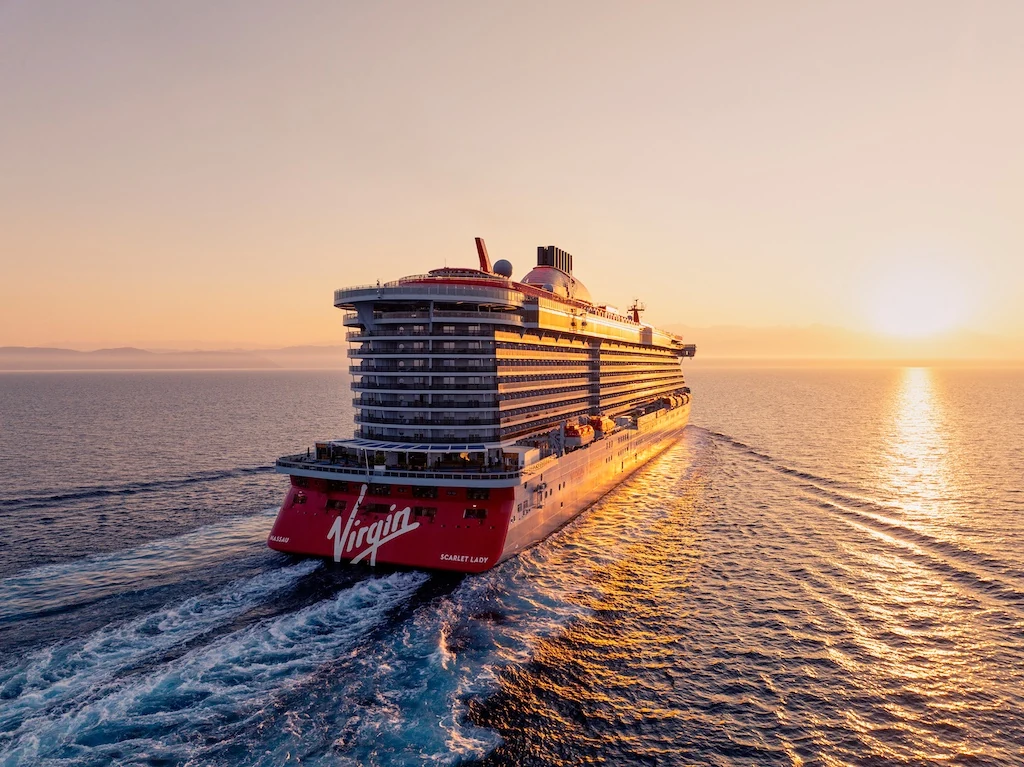 Virgin Voyages' Scarlet Lady sailing at golden hour, luxury adults-only cruising booked by Travel Squad Vacations